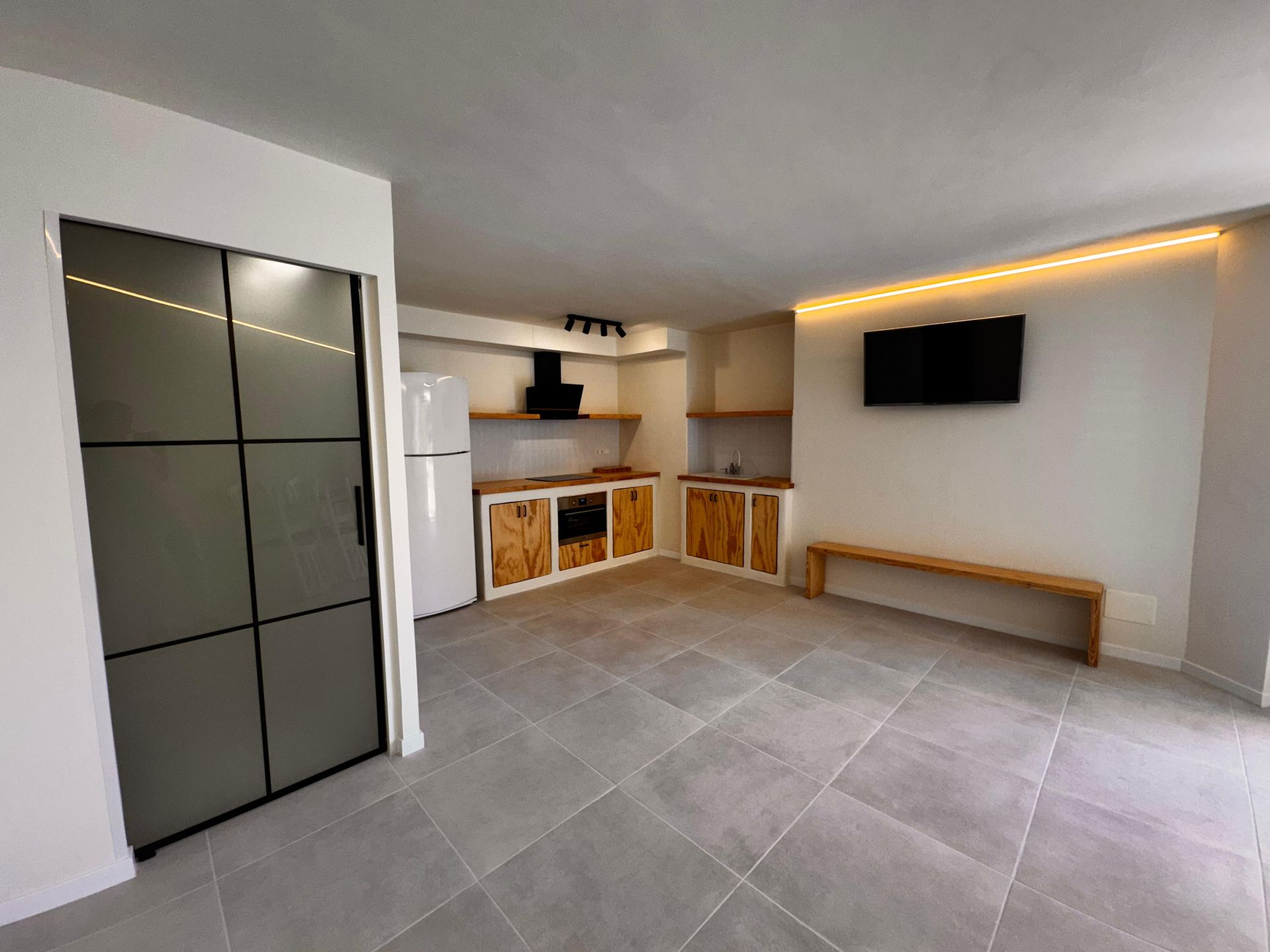 Moderna cocina abierta con gabinetes de madera rústica, puerta de acero inoxidable y TV montada.