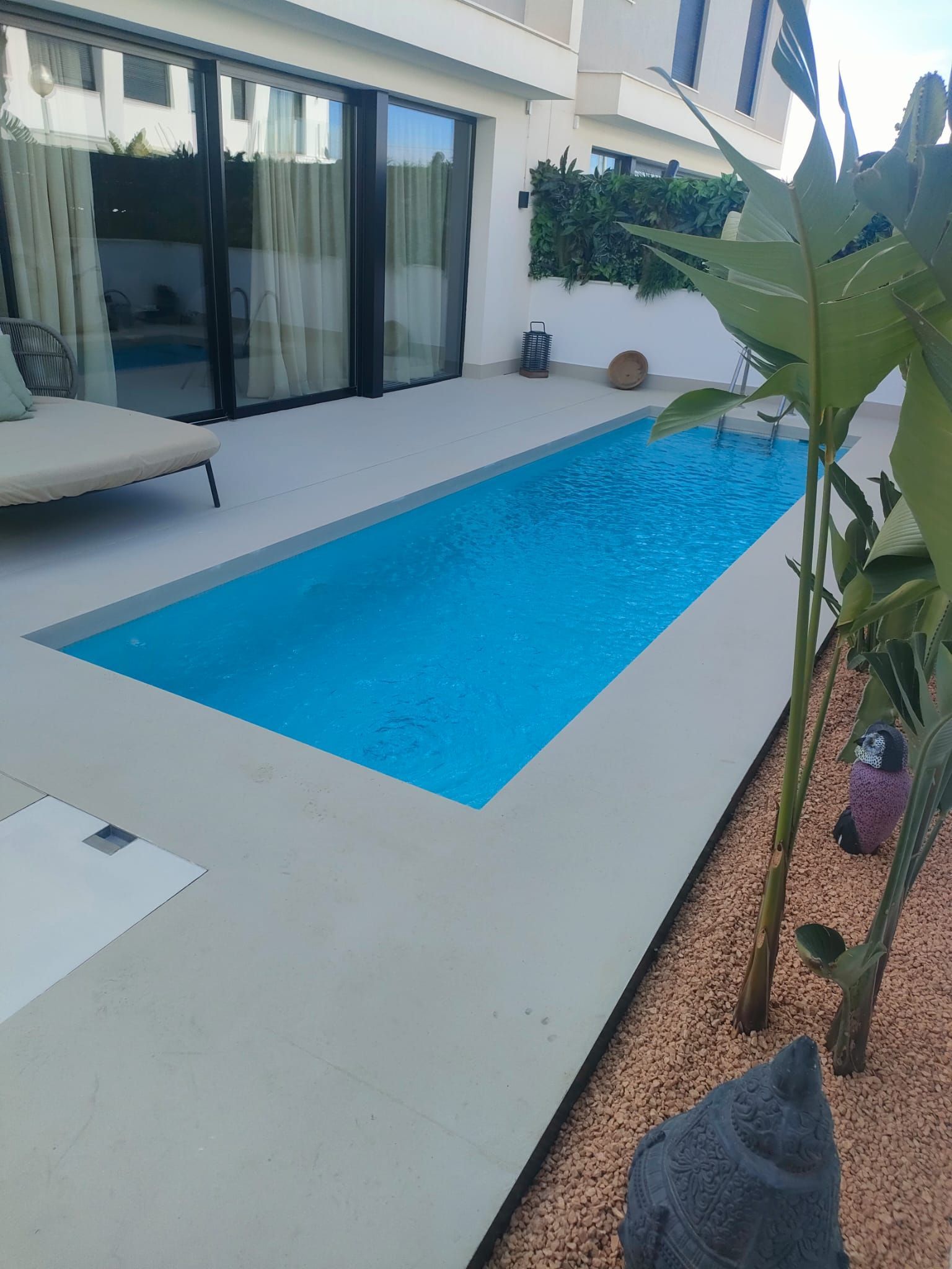 Una piscina larga y estrecha fuera de una casa moderna con un interior azul brillante.