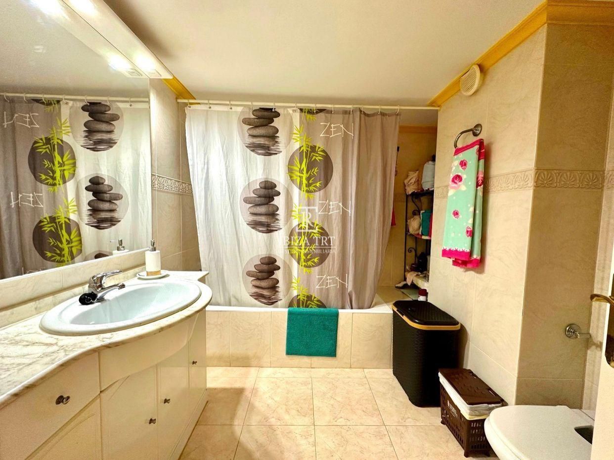 Baño con bañera, lavabo y cortina de ducha decorativa con piedras apiladas.