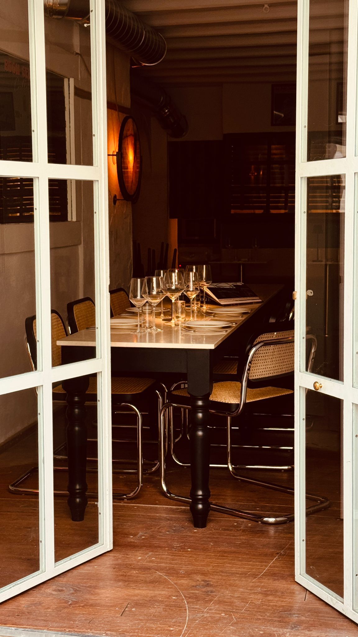 Vista a través de puertas francesas blancas abiertas de una mesa de comedor iluminada con velas preparada para una comida.