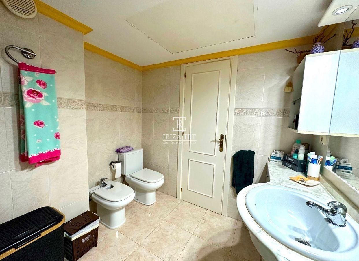 Baño con inodoro, bidé, lavabo y mueble de pared. Paredes, puerta y toallas en tonos claros.