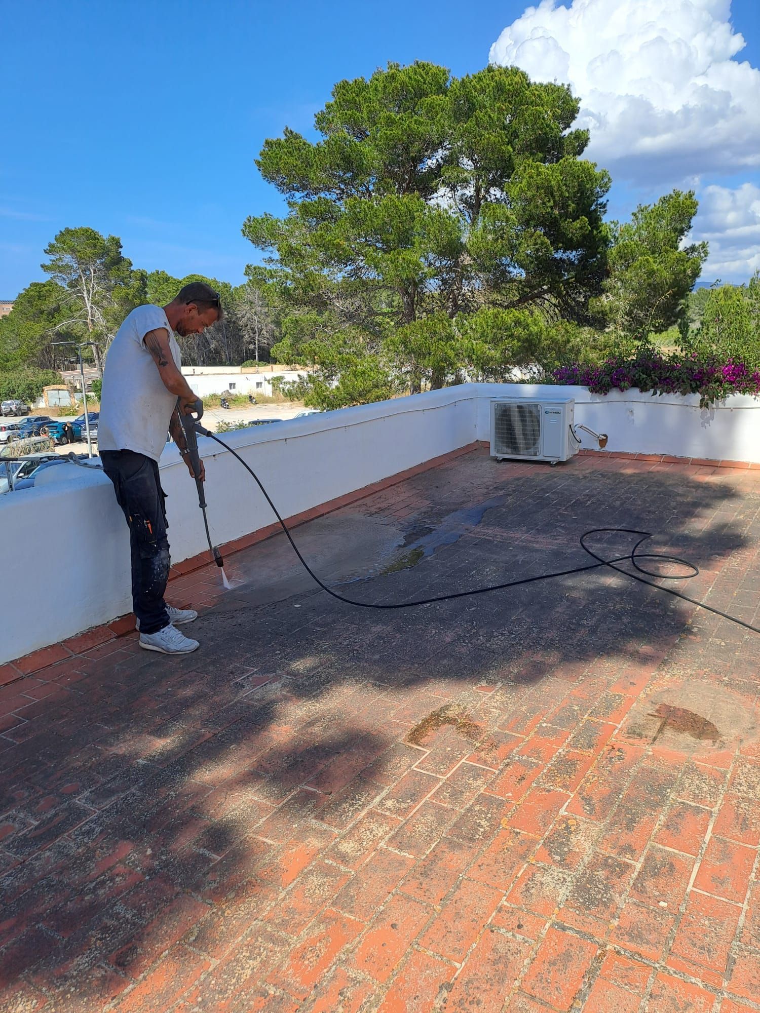 Mano de obra lavando un techo de tejas rojas en un día soleado, con una manguera de agua.