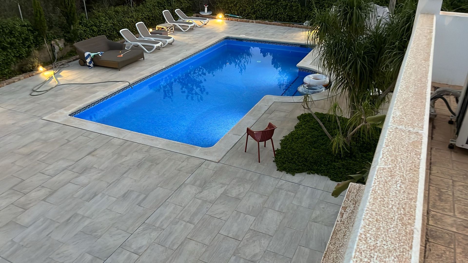 Área de piscina con agua azul, camastros y patio pavimentado.