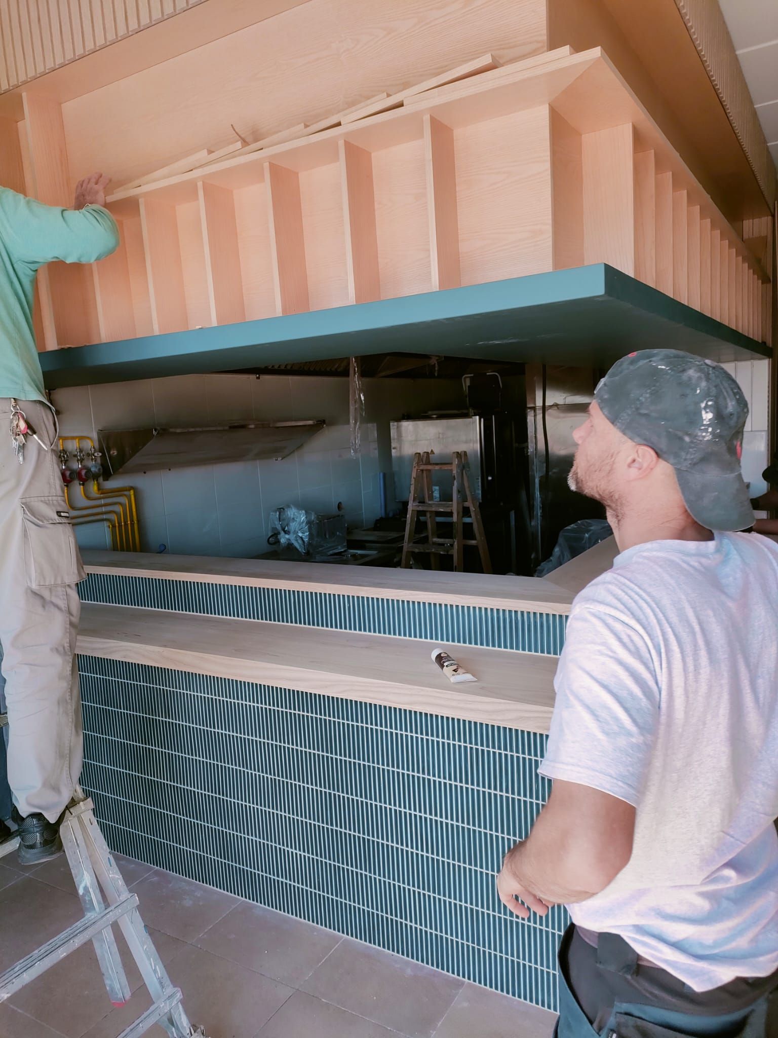 Dos trabajadores construyen un bar con fachada con dibujos de ondas azules y estructuras de color melocotón.