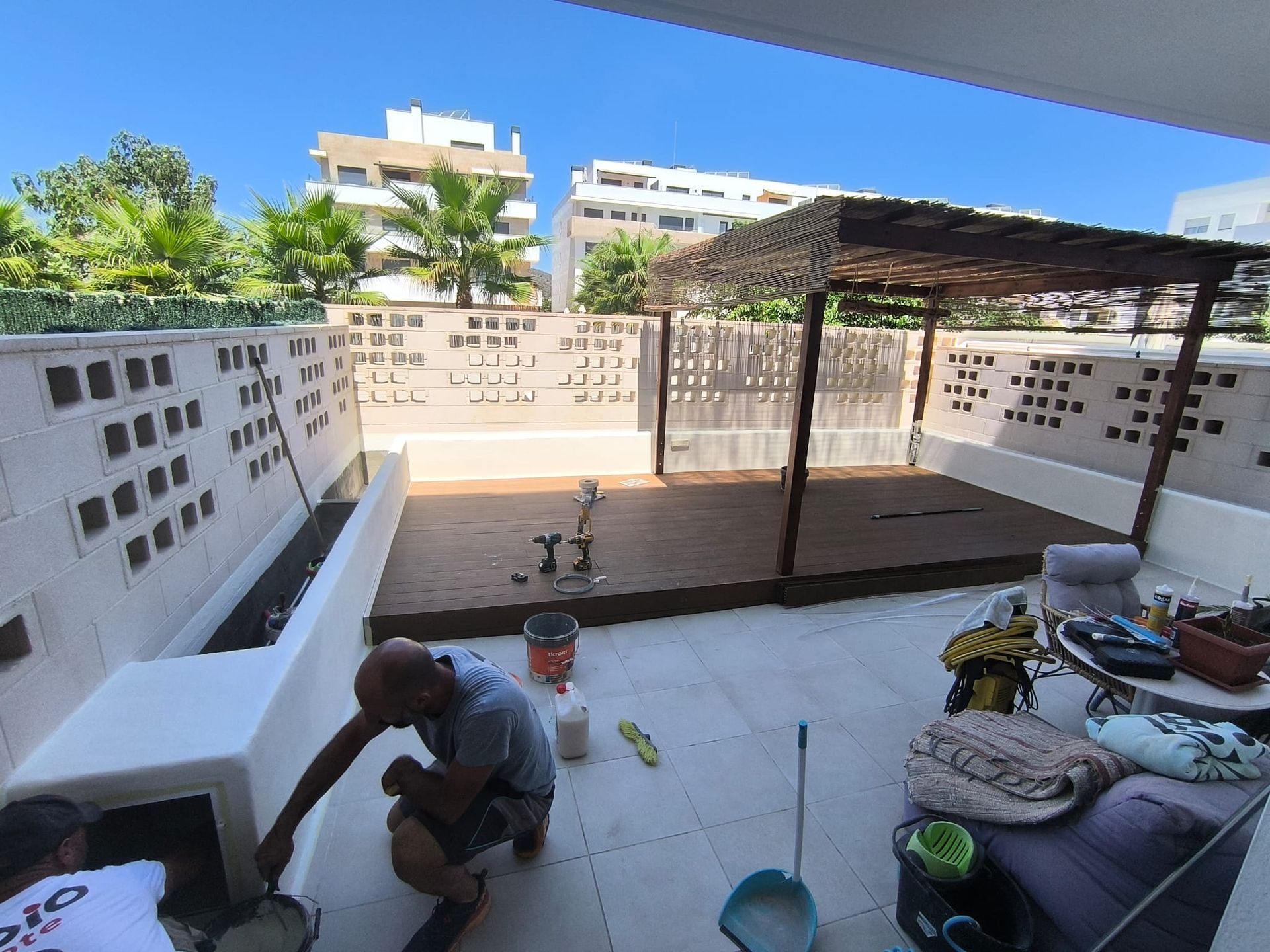 Dos hombres trabajando en un tejado de color claro con una estructura de madera a la sombra en un día soleado.