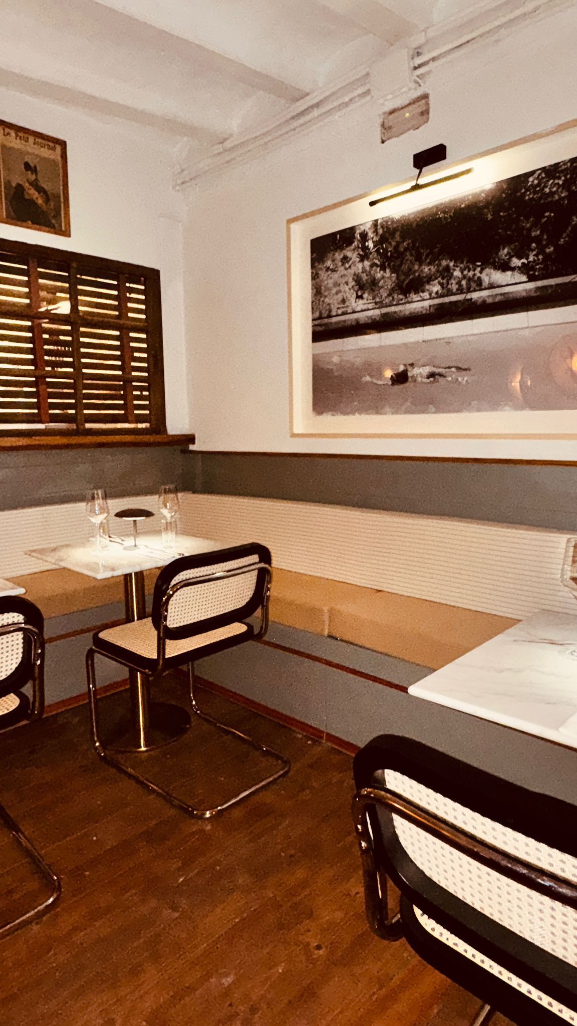 Cabina de restaurante con sillas, mesa y ventana. Fotografía en blanco y negro en la pared. Suelo de madera y persianas.