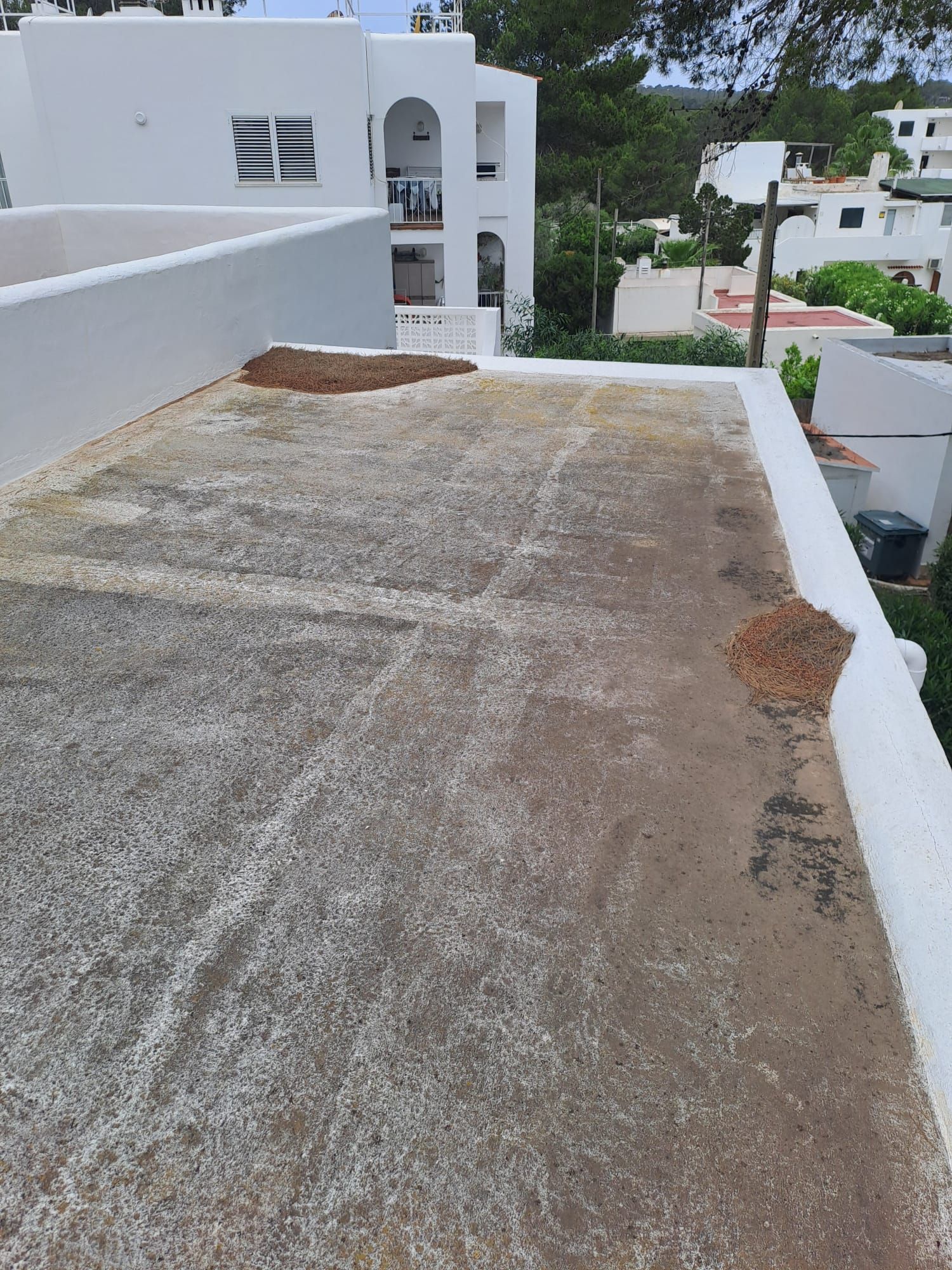 Azotea plana con escombros marrones, edificio blanco al fondo, exterior soleado.