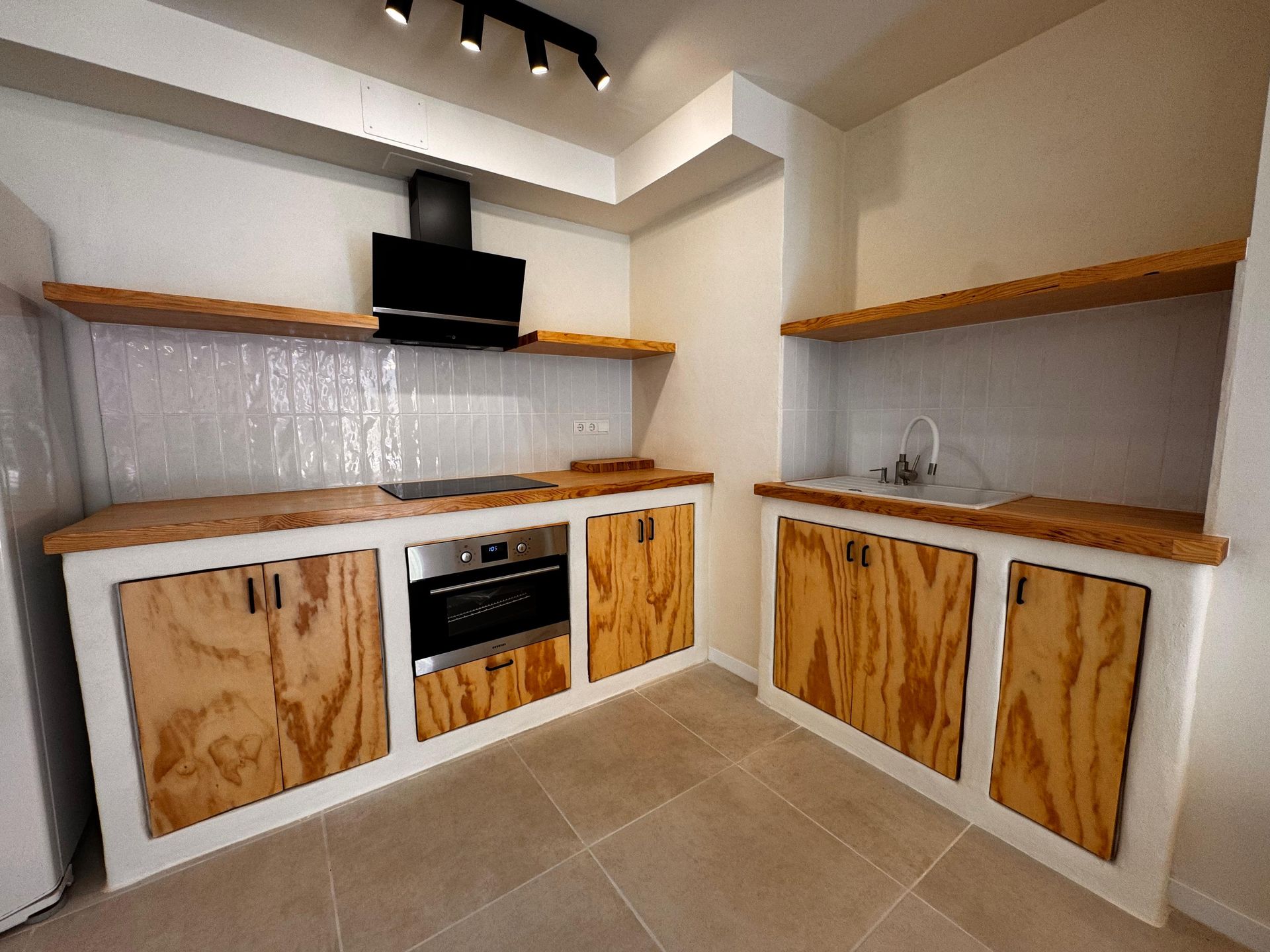 Cocina moderna con gabinetes y encimeras de madera, salpicadero de azulejos y paredes blancas.