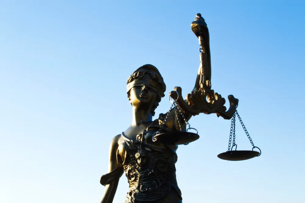 Estatua de la Dama de la Justicia sosteniendo una balanza, contra un cielo azul.