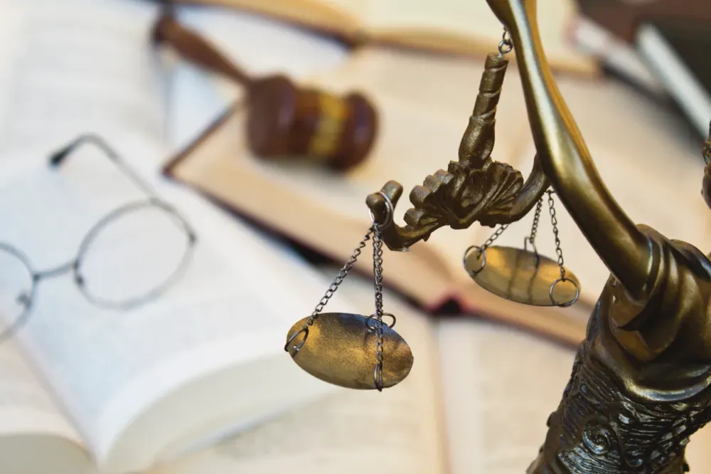 Estatua de la Justicia sosteniendo una balanza, junto a libros, un mazo y gafas.