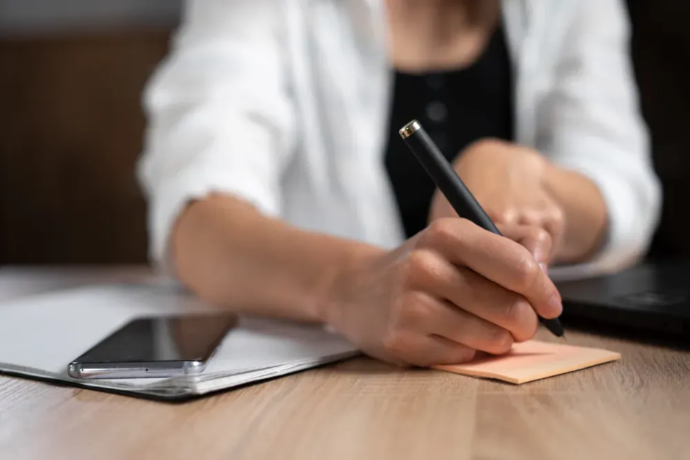 Manos escribiendo notas, computadora portátil, contrato, mazo, bolígrafo sobre una mesa blanca.