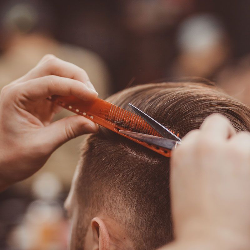 Ein Mann lässt sich von einem Friseur mit Schere und Kamm die Haare schneiden