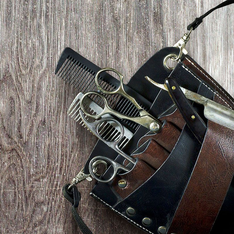 Ein Kamm, eine Schere und ein Rasierer liegen in einem Lederetui auf einem Holztisch.