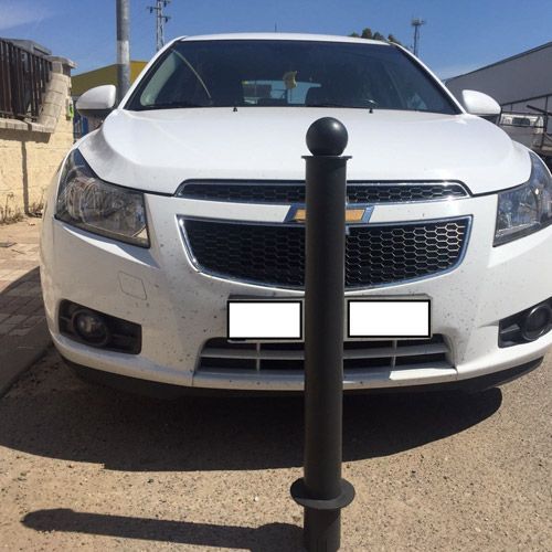 Un coche blanco está aparcado junto a un poste negro.