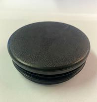 Una tapa de plástico negra reposa sobre una superficie blanca.