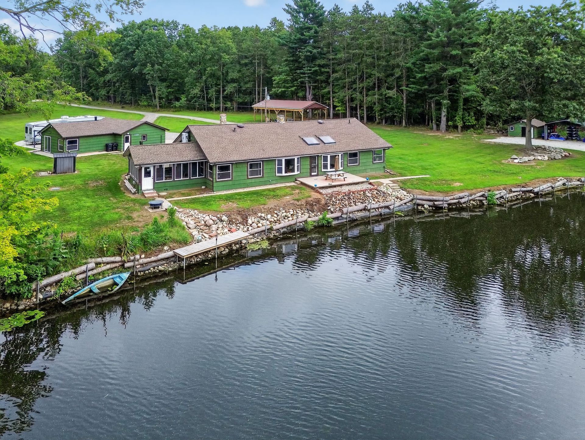 Green lakeside building with dock, grassy yard, trees, and dark water.