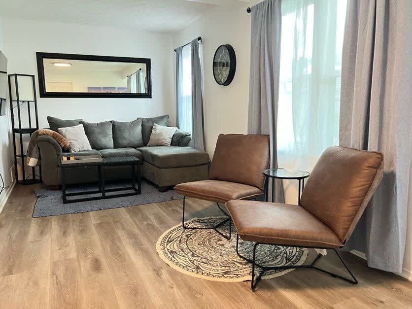 Living room with gray sofa, brown chairs, mirror, clock, and wood-look flooring.