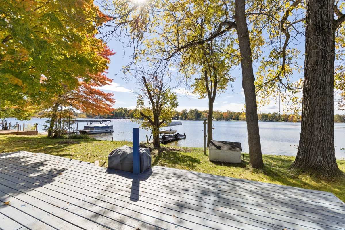 Lakeside view with fall foliage, a deck, boat docks, and a sunny sky.