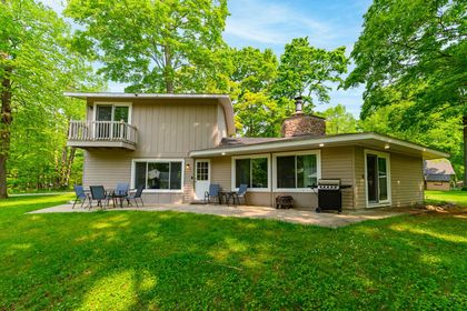 A large log cabin with a large deck in the middle of the woods.