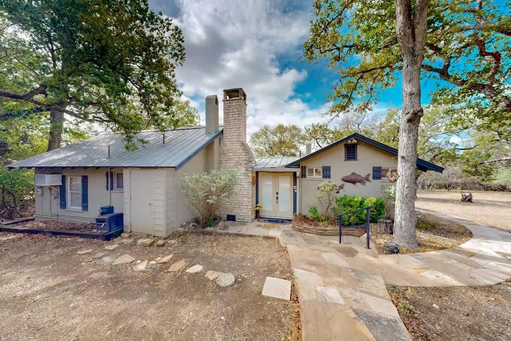 Rustic house with stone chimney, surrounded by trees under a cloudy sky.