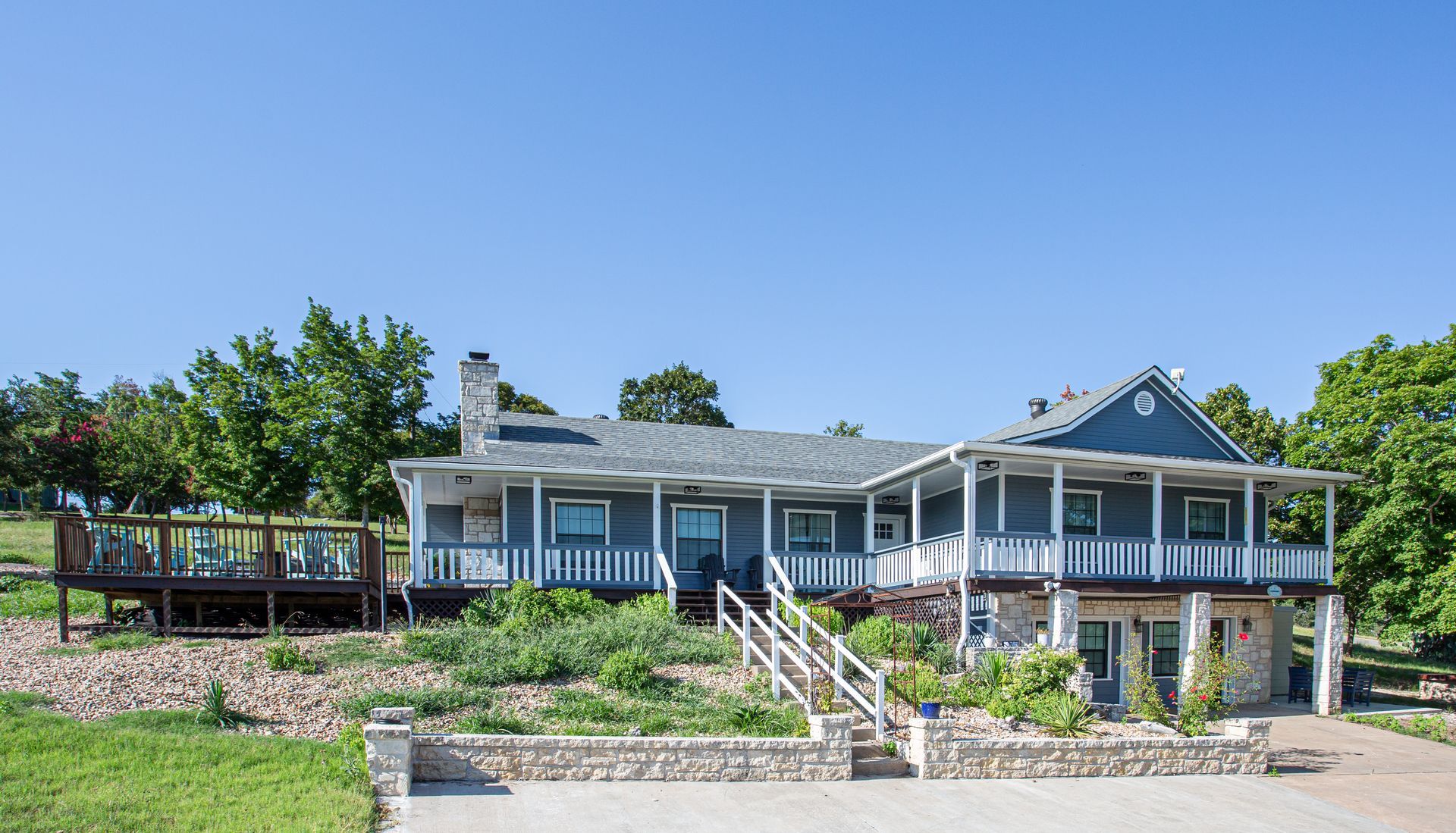 Two-story blue house with porch, deck, and stone foundation against a clear sky.