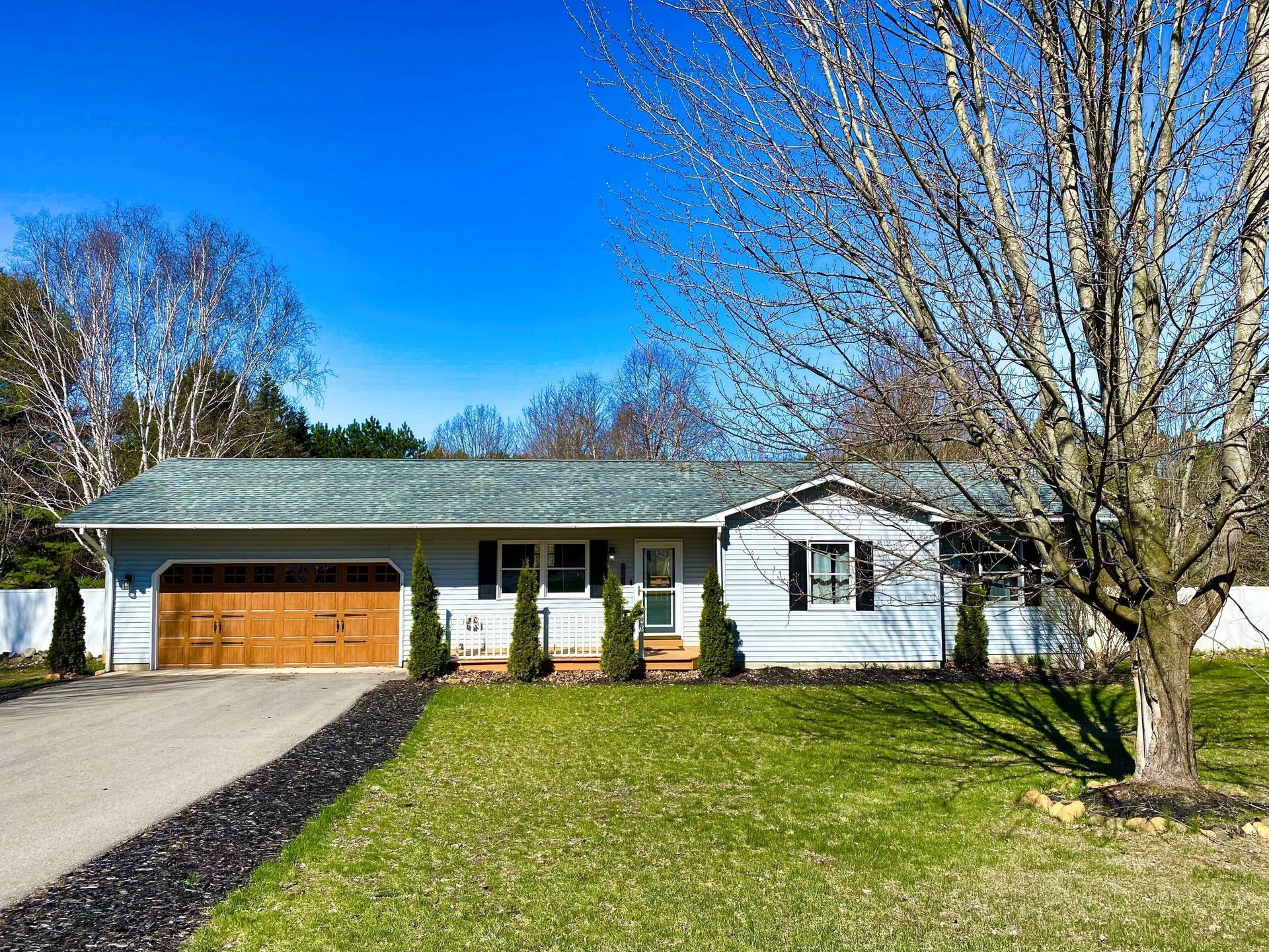 Ranch-style house with gray siding, a brown garage door, and a green lawn on a sunny day.