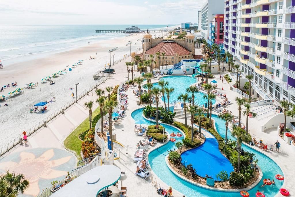 An aerial view of a large swimming pool surrounded by palm trees next to a beach.