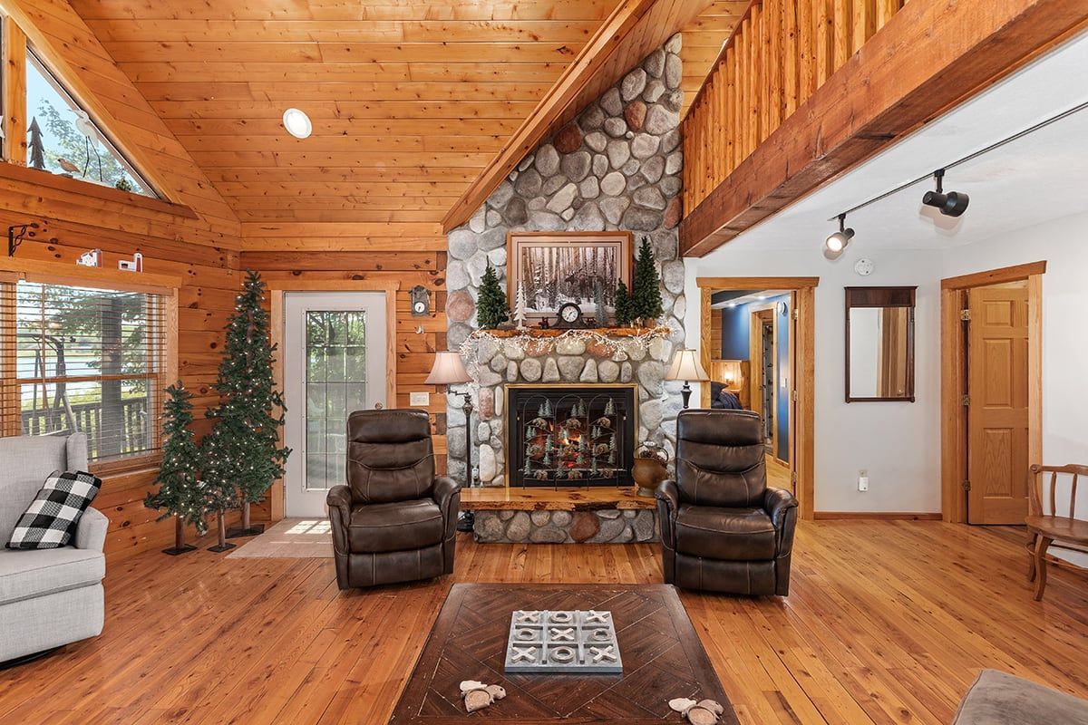 A living room in a log cabin with a fireplace and chairs.