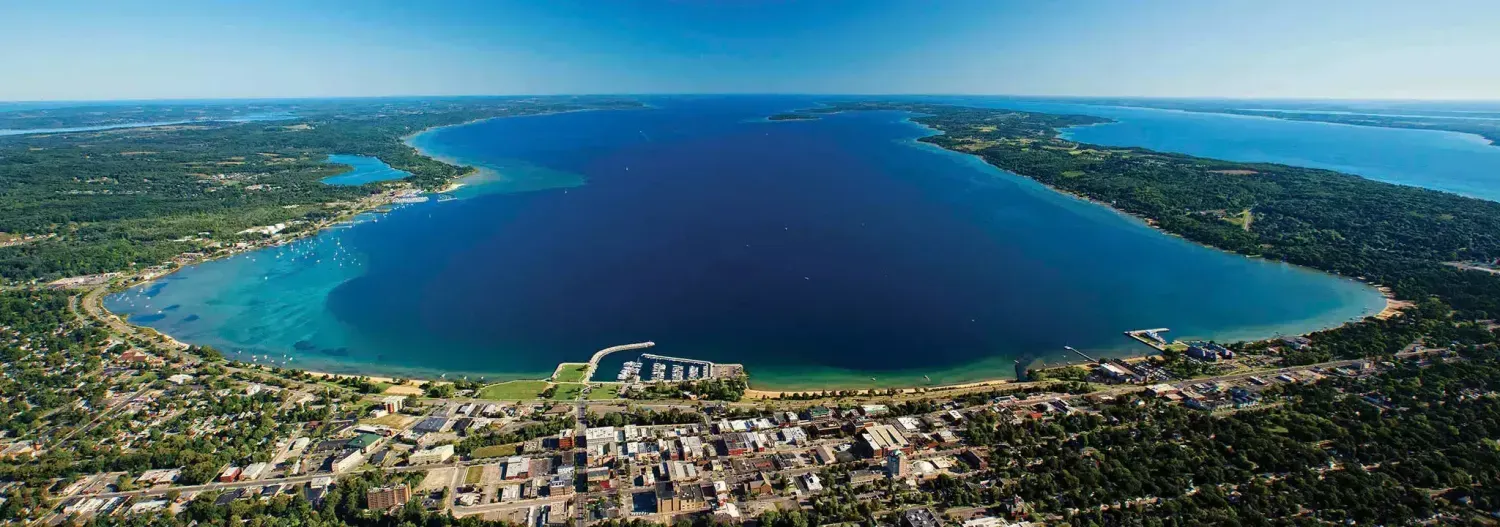 Aerial view of a town on a shoreline next to a large blue lake under a clear blue sky.