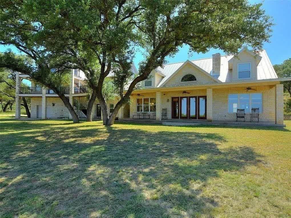 Stone house with porch, large tree in front, sunny day.