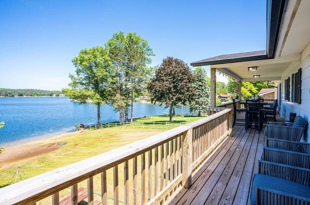 Wooden deck overlooking a lake, with trees and a blue sky in the background.
