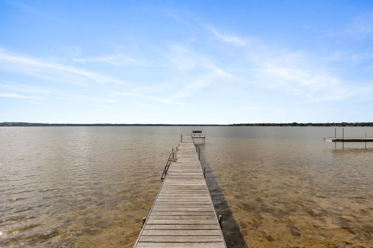 Wooden pier extending into calm water under a blue sky.