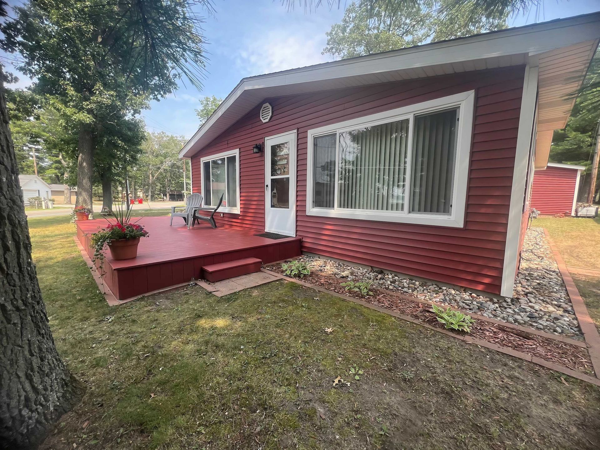 Red-sided cottage with a deck, large windows, and a small garden bed along the side.