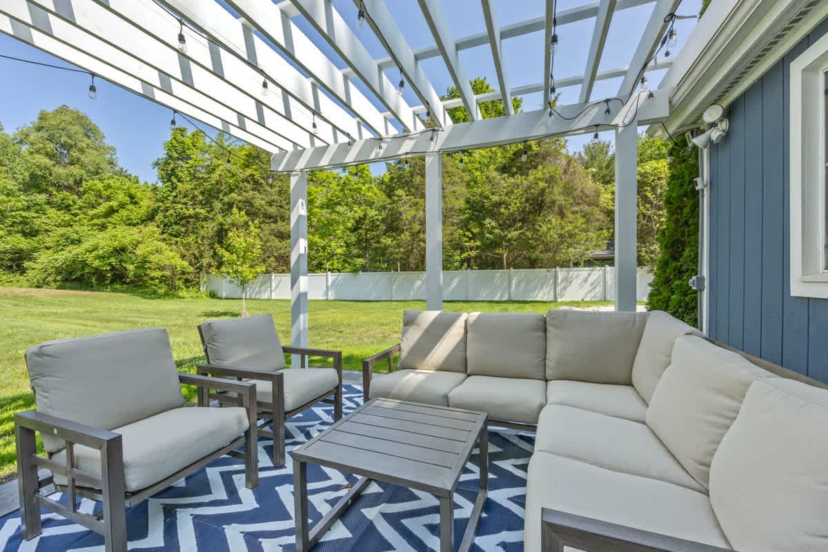 Patio with sectional sofa, armchairs, and coffee table under a white pergola on a blue and white patterned rug.
