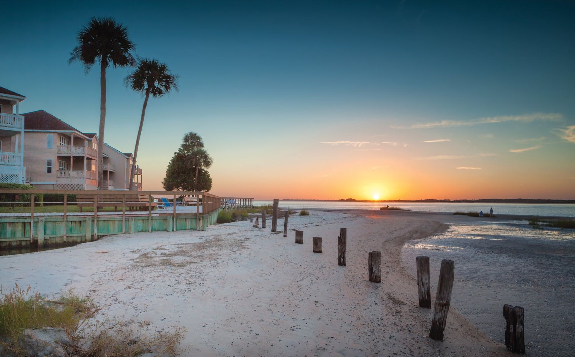 A sunset over a beach with palm trees and houses in the background