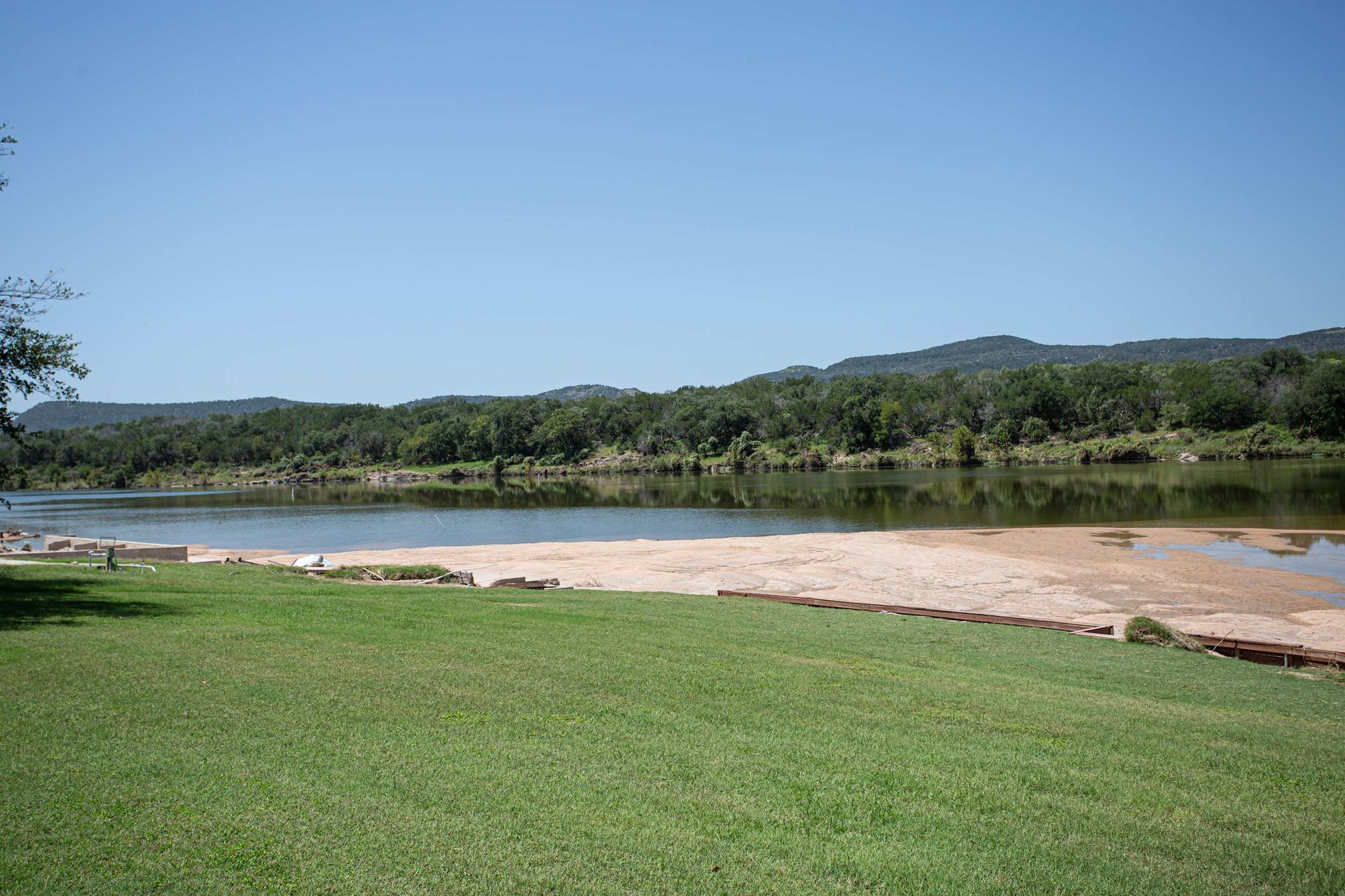A row of lounge chairs on a sandy beach next to a lake.