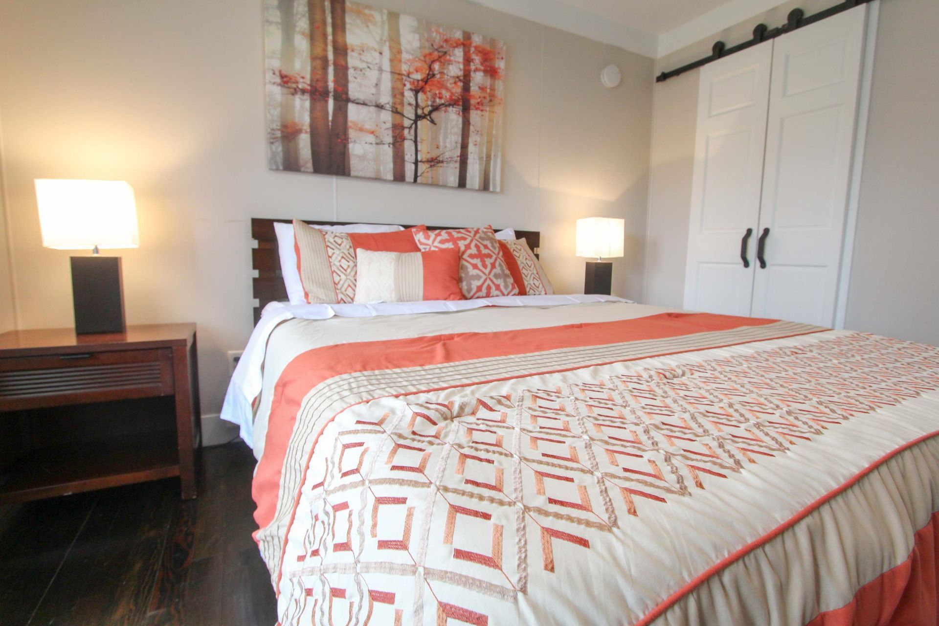 Bedroom with a made bed, nightstands with lamps, and a decorative painting above. A white wardrobe is on the right.