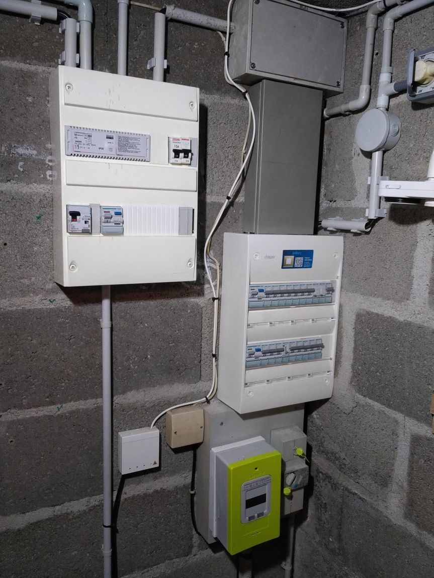 Compteurs des services publics et tableaux électriques fixés sur un mur en parpaings dans un local technique au sous-sol