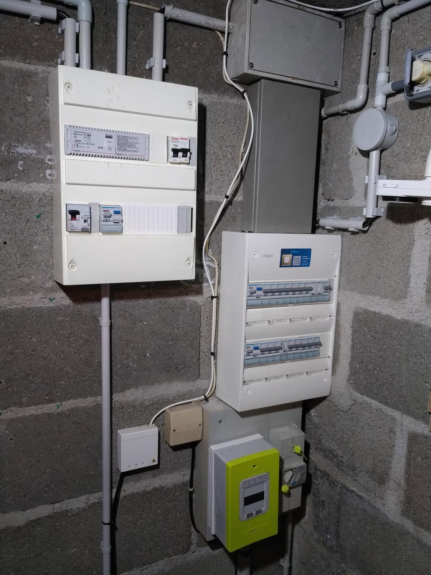 Tableaux électriques et compteurs fixés à un mur en parpaings gris dans un local technique