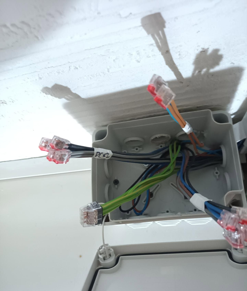 Boîte de dérivation ouverte avec des fils multicolores et des connecteurs apparents au plafond blanc