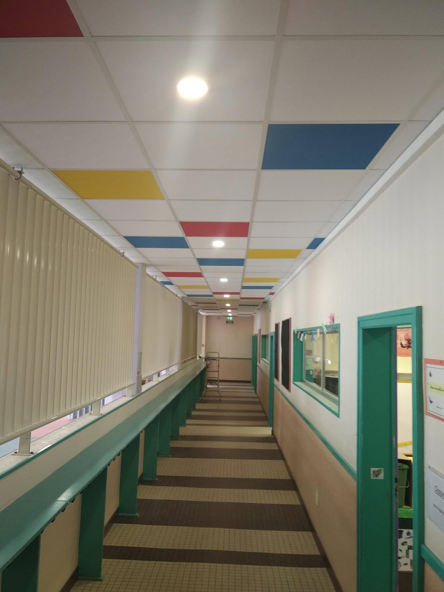 Couloir vide avec une moquette à rayures, des murs turquoise et des dalles de plafond colorées.