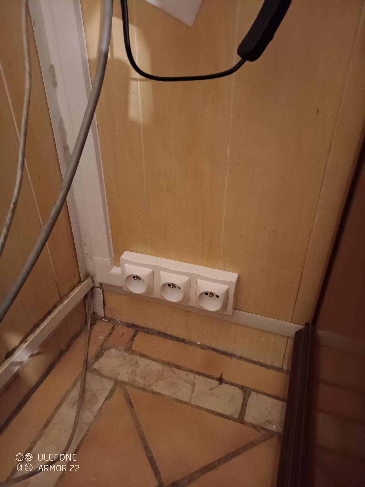Prises électriques au ras du sol sous un meuble, avec un sol carrelé.