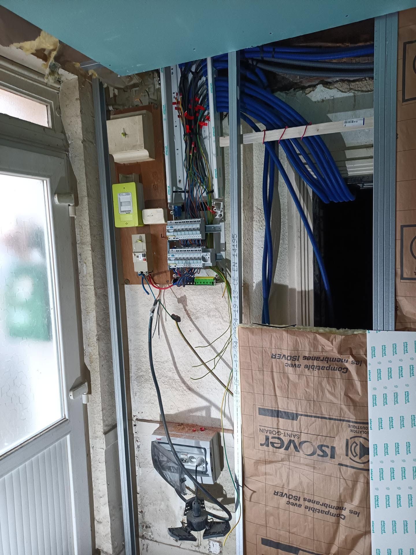 Placard technique endommagé, avec des fils électriques apparents, des câbles qui pendent et de l’isolant à l’intérieur d’une embrasure de porte
