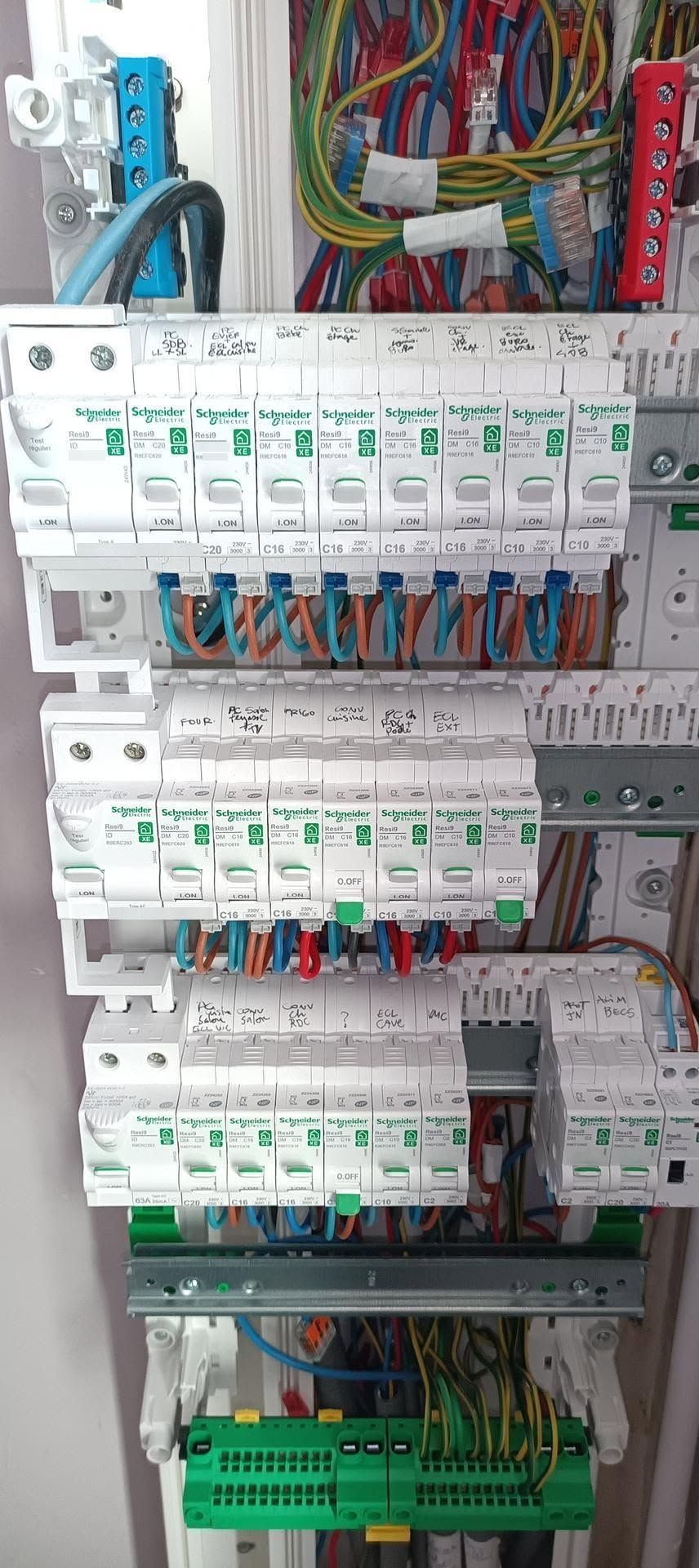 Armoire électrique avec des rangées de disjoncteurs blancs, des fils multicolores et des borniers verts