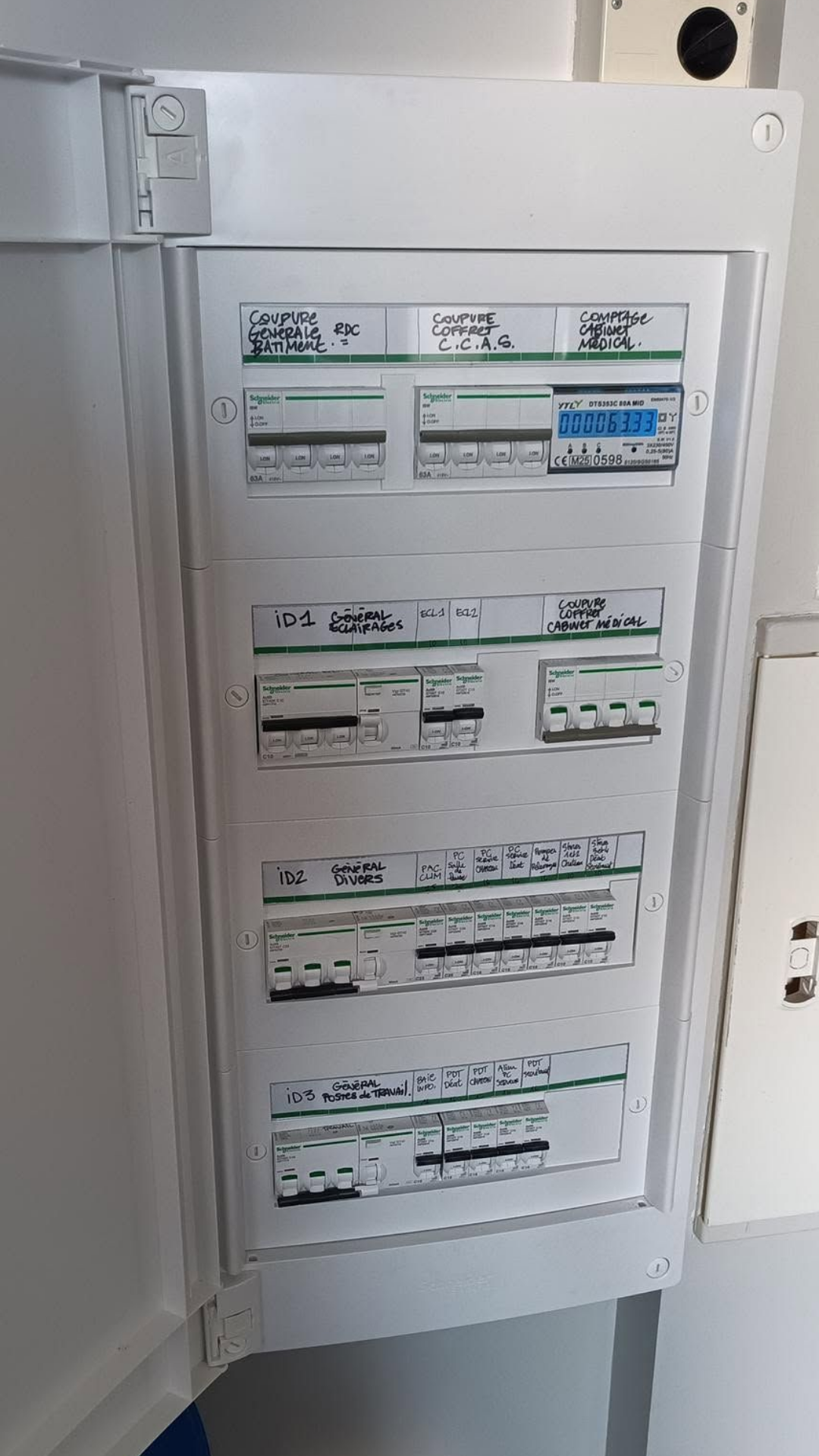 Tableau électrique avec ses disjoncteurs étiquetés dans une armoire blanche.