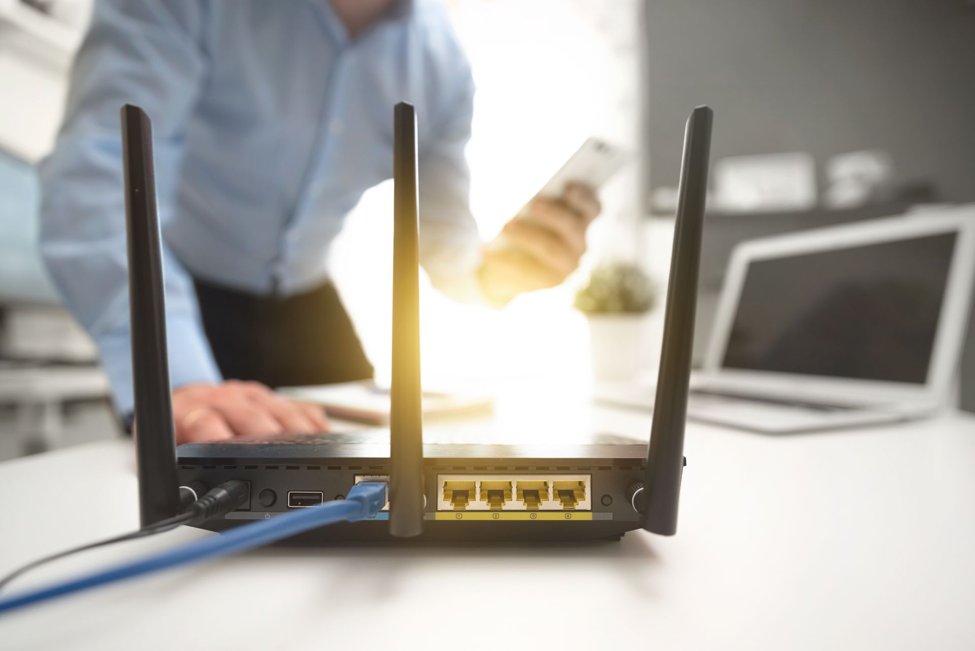 Routeur Wi-Fi avec antennes posé sur un bureau, personne travaillant sur un ordinateur portable et arrière-plan flou