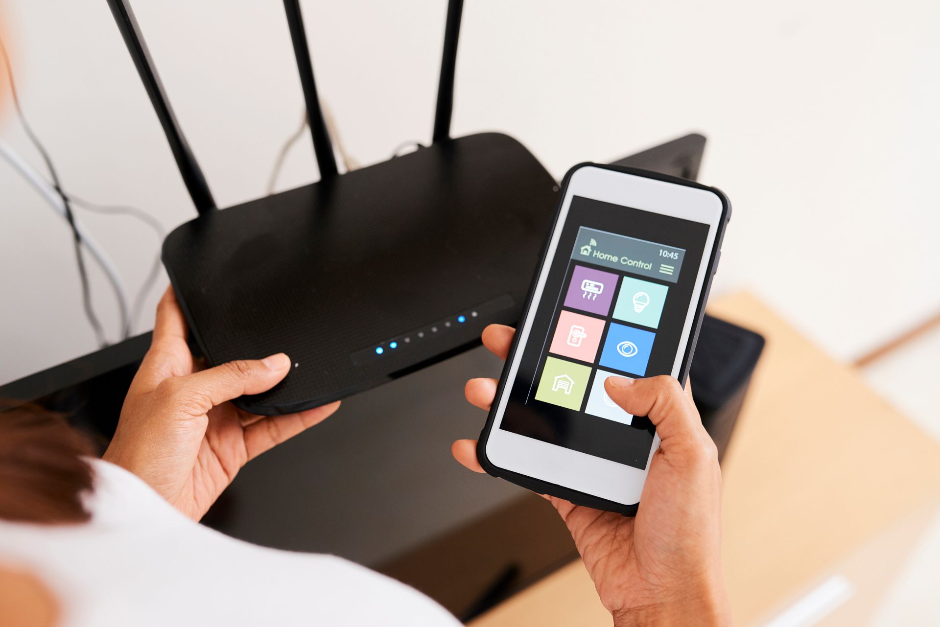 Personne tenant un smartphone près d’un routeur Wi-Fi noir avec des voyants lumineux et des antennes, posé sur une table