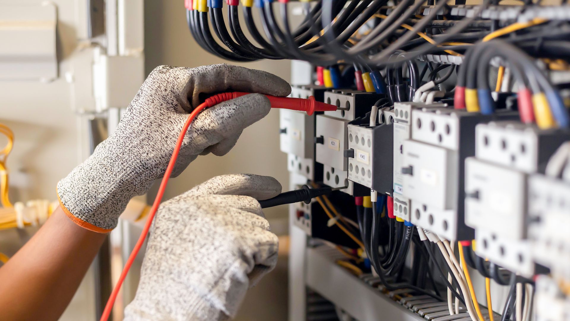Des mains gantées testent le câblage à l’intérieur d’un tableau électrique avec une sonde rouge