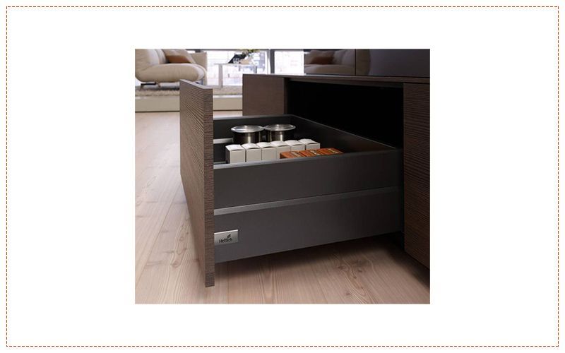 Un cajón de cocina lleno de ollas y sartenes sobre un piso de madera.