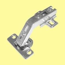 Un primer plano de una bisagra de puerta de gabinete de acero inoxidable sobre un fondo amarillo.